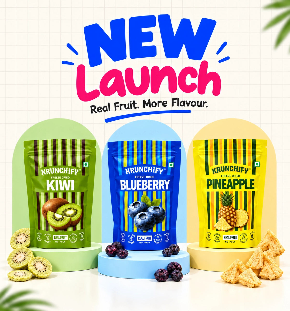 Three stand-up pouches of Krunchify freeze dried fruits are displayed on colorful pedestals with promotional text above. The pouches are Kiwi (green), Blueberry (blue), and Pineapple (yellow), with kiwi slices, blueberries, and pineapple crisps arranged around them on a white grid background.